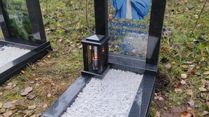 Гранитная лампада зажжённой свечой рядом со стеклянным памятником с прозрачным фоном